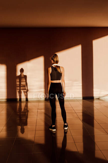 Vue arrière de debout anonyme jeune femme caucasienne athlétique au coucher du soleil, ombres et lumière sur le fond — Photo de stock