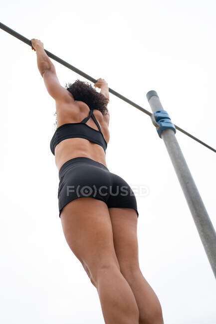 From below unrecognizable fit female athlete doing muscle up exercise on bar during workout against gray sky — Stock Photo
