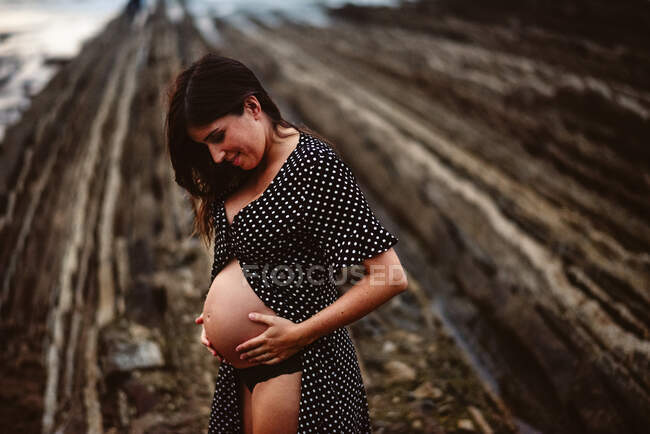 Vue latérale femme enceinte réfléchie debout sur un rocher rugueux près de la mer dans la nature — Photo de stock
