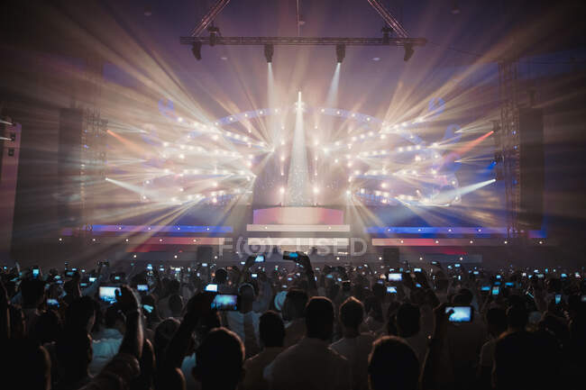 Visão traseira da multidão em pessoas irreconhecíveis tirando fotos em smartphones durante concerto ao vivo na arena escura — Fotografia de Stock