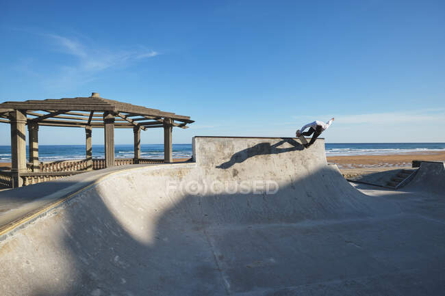 Unrecognizable teen boy in riding skateboard in skate park on sunny day on seashore — Stock Photo