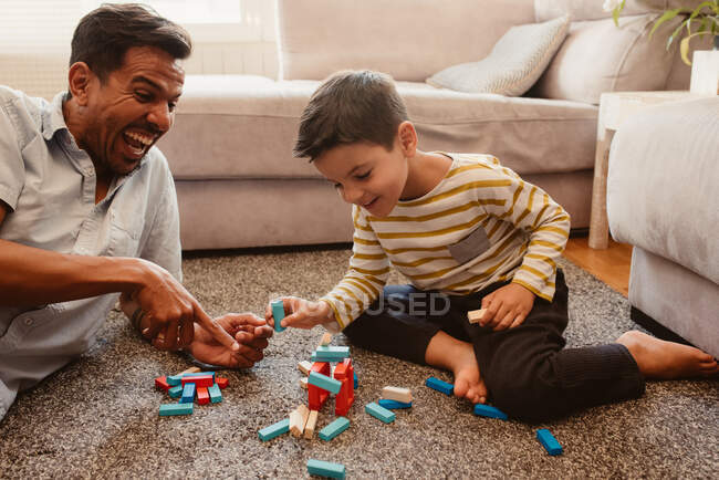 Vista lateral de padre e hijo jugando con piezas de construcción en el comedor de la casa - foto de stock