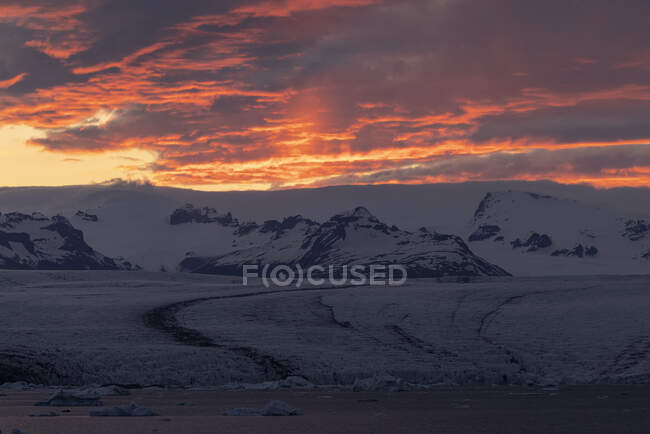 Cume de montanha nevado localizado contra o céu brilhante nublado sol laranja na noite de inverno na Islândia — Fotografia de Stock