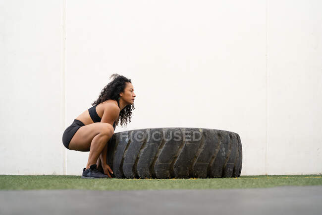 Vue latérale d'une athlète féminine asiatique musclée retournant un pneu lourd pendant un entraînement intense — Photo de stock