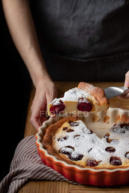 Persona sin rostro de pie en la mesa con trozo de pastel sabroso cortado con cerezas - foto de stock