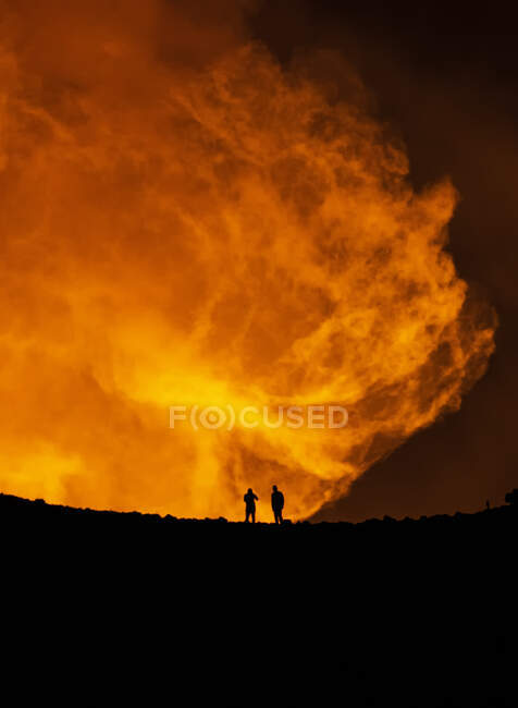 Silhouette di viaggiatori anonimi in piedi contro il fumo arancione del vulcano attivo in Islanda — Foto stock