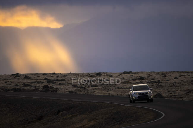Современный автомобиль едет по извилистой дороге через природу против облачного неба восхода солнца в Исландии — стоковое фото