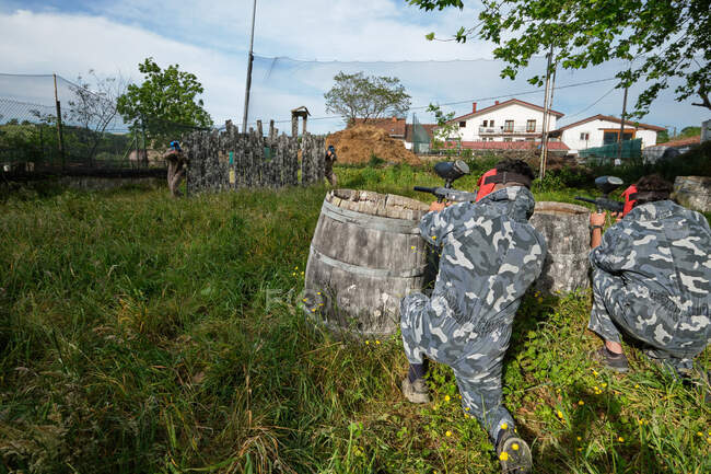 Unrecognizable team players in camouflage wear and with guns aiming at each other while playing paintball — Stock Photo