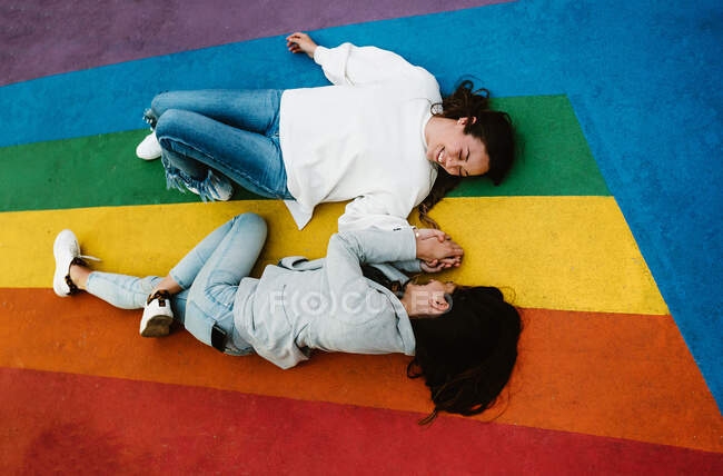 De cima alegres jovens namoradas homossexuais deitado perto do arco-íris colorido chão e se divertindo — Fotografia de Stock