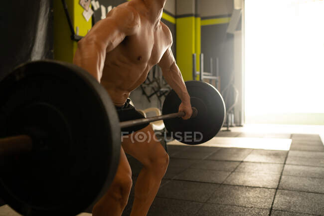 Вид збоку на урожай анонімний спортсмен чоловічої статі з голим торсом, що виконує вправи з важким штангою під час інтенсивних тренувань у спортзалі — стокове фото