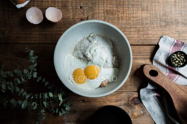 Von oben Schüssel mit Eiern und Sahne vermischt mit Semmelbröseln und Mehl auf Holztisch während der Teigzubereitung — Stockfoto