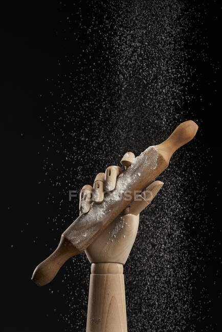 Rolling pin in flour in wooden hand on black background in studio showing concept of culinary — Stock Photo