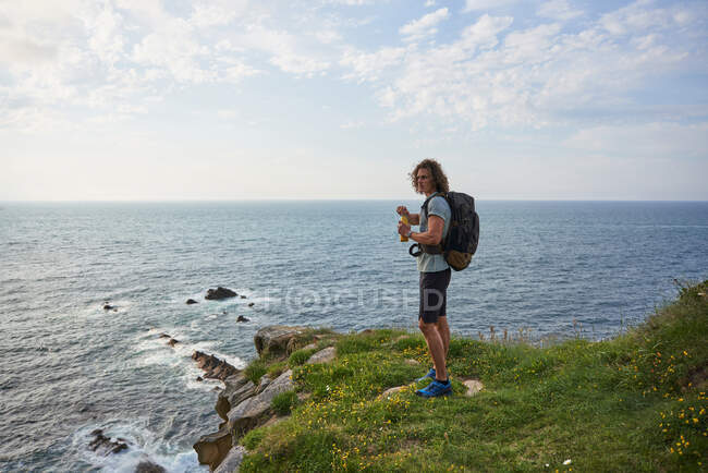 Vista laterale dell'escursionista maschio in piedi e acqua potabile sullo sfondo del cielo e del mare durante il trekking in estate — Foto stock