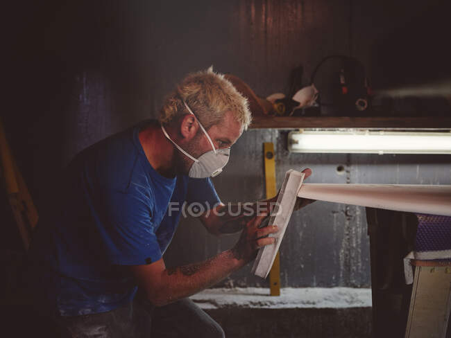 Hombre en respirador con equipo lijado escritorio blanco en el lugar de trabajo - foto de stock