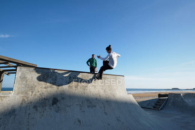 Irreconocible adolescente montar monopatín en skate park en día soleado en la orilla del mar - foto de stock
