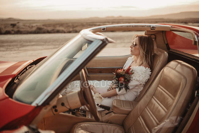 Frau in elegantem weißen Kleid sitzt auf dem Beifahrersitz eines Luxusfahrzeugs während einer Roadtrip durch den Naturpark Bardenas Reales in Navarra, Spanien — Stockfoto