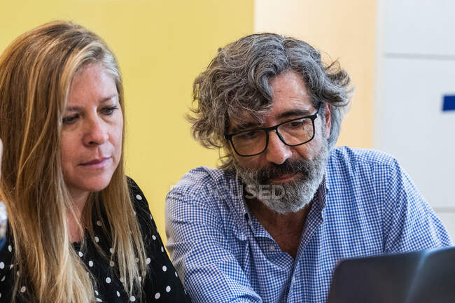 Focused mature colleagues sitting at table and using netbook while working on new project at workplace — Stock Photo