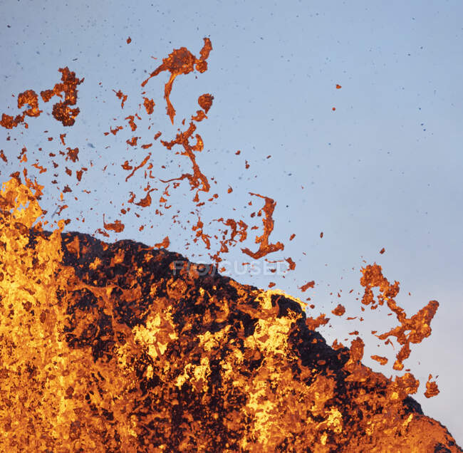 Salpicaduras de lava naranja caliente en erupción desde el pico de la montaña volcánica rodeado en Islandia - foto de stock