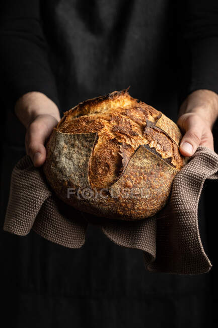 Unrecognizable crop chef in apron standing with piece of freshly baked bread — Stock Photo