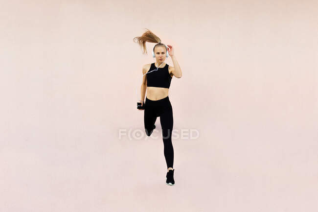 Young athletic caucasian woman wearing headphones and sport outfit, jumping against bright background outdoors — Stock Photo