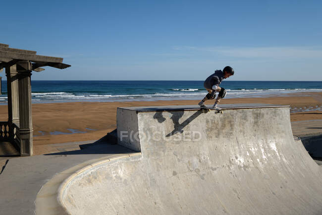 Невпізнаваний хлопчик-підліток в захисному шоломі катається на скейтборді в скейт-парку в сонячний день на березі моря — стокове фото