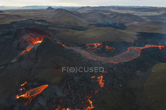 Drone view of stream of hot orange lava flowing through mountainous terrain in morning in Iceland — Stock Photo