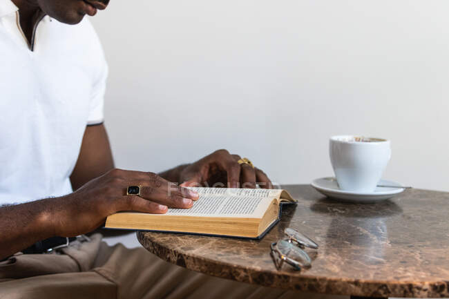 Чорний дорослий чоловік у звичайному одязі читає цікавий роман у яскравому кафе. — стокове фото