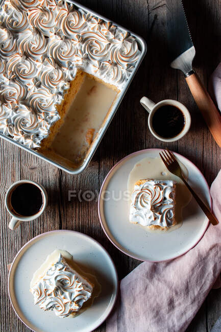 D'en haut trois laits gâteau dans un plat de cuisson et des assiettes avec des tasses de café fort sur une table en bois — Photo de stock