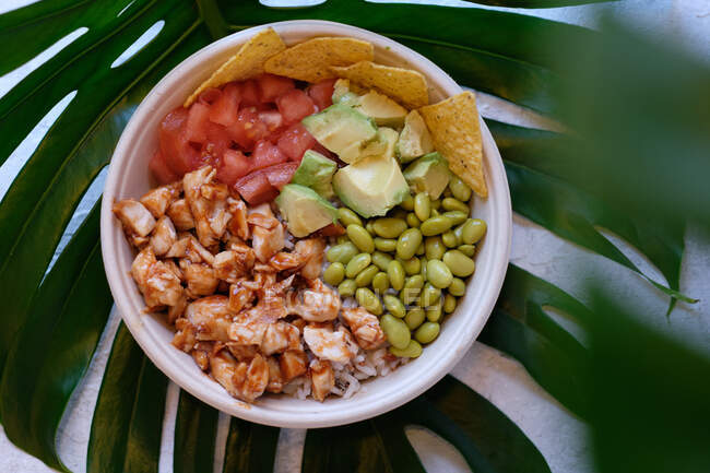 Vue du dessus de bol de riz hawaïen appétissant avec poulet saucy et avocat servi avec des haricots de tomates fraîches et des nachos — Photo de stock