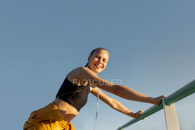 Jeune femme caucasienne athlétique gaie penchée sur la rampe à l'extérieur et regardant la caméra après l'entraînement — Photo de stock