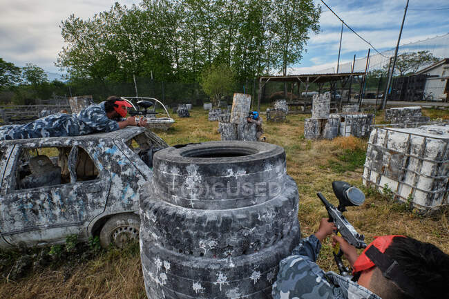 Unerkennbare männliche Spieler im Tarnkostüm spielen Paintball zwischen alten verlassenen Transportmitteln und Müll — Stockfoto