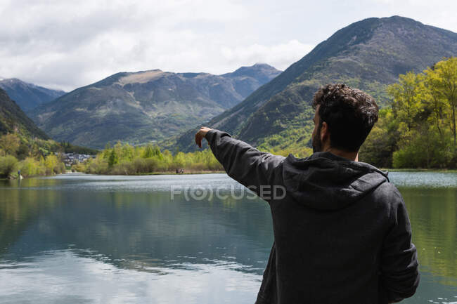 Повернення до нерозпізнаного чоловіка - мандрівника, що сидить на пірсі біля ставка і має свободу вказувати на гори на гірському хребті Піренеїв. — стокове фото