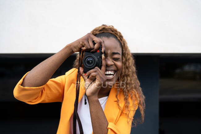 Happy African American female laughing happily with mouth opened while taking picture on photo camera — Stock Photo