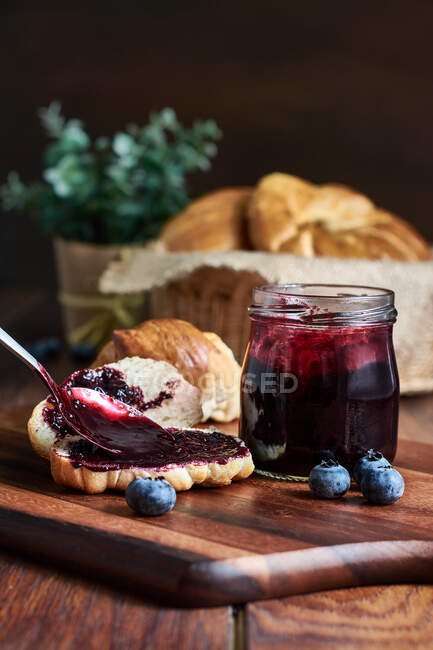 Preparazione di una colazione di croissant con marmellata di mirtillo su un tavolo di legno — Foto stock