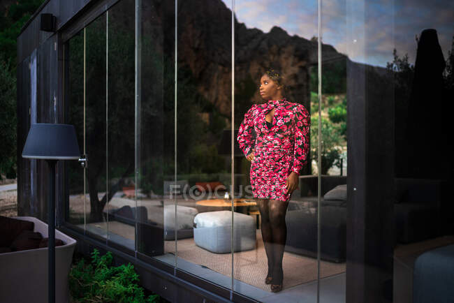 Donna afroamericana in abito e scarpe con tacco alto in piedi vicino alla finestra in camera d'albergo situato in località montagnosa — Foto stock