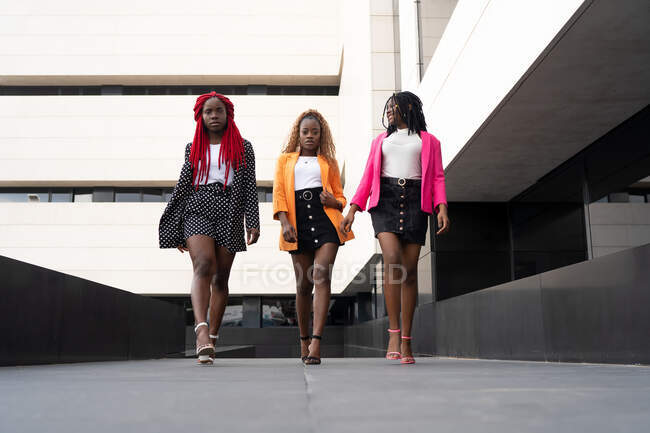 Рівень землі повний тіла афроамериканських жінок в стильній сукні роблять злітно-посадкову смугу ходити разом поруч із сучасною будівлею. — стокове фото
