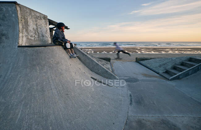 Невідомі активні фігуристи катаються на скейтбордах в скейтборді біля моря на заході сонця влітку — стокове фото