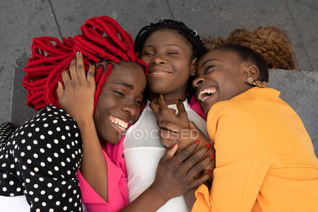 Высокий угол расположения афроамериканских подруг, лежащих вместе и обнимающих друг друга, веселясь — стоковое фото