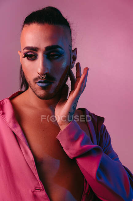 Portrait de femme barbu transgenre glamour dans un maquillage sophistiqué posant sur fond rose au studio détournant les yeux — Photo de stock