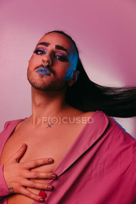 Портрет гламурної трансгендерної бородатої жінки у витонченому макіяжі позує на рожевому тлі на студії, дивлячись на камеру — стокове фото