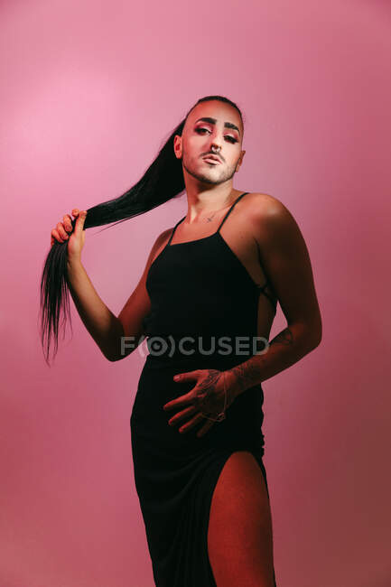 Porträt einer glamourösen Transgender-bärtigen Frau in raffiniertem Make-up, die vor rosa Hintergrund im Studio vor der Kamera posiert — Stockfoto