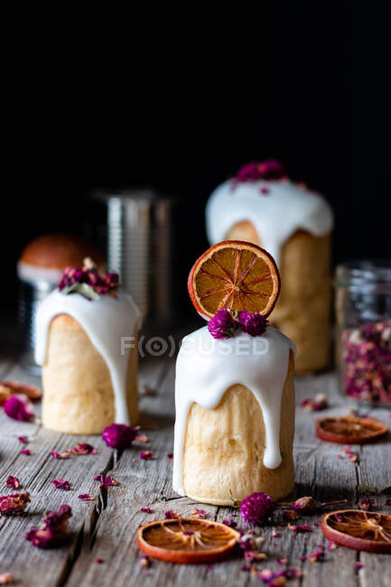 Plusieurs délicieux kulichs faits maison coulés avec glaçure douce et décorés de morceaux d'orange sec et de fleurs sur une table en bois — Photo de stock