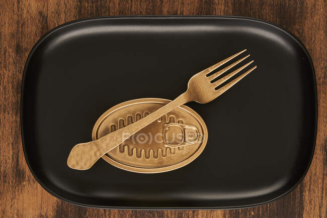 Top view of golden fork placed near sealed canned food on rectangular black tray — Stock Photo