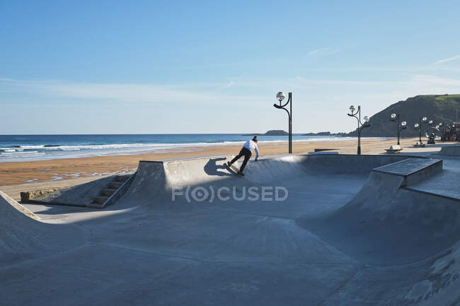 Unrecognizable teen boy riding skateboard in skate park on sunny day on seashore — Stock Photo