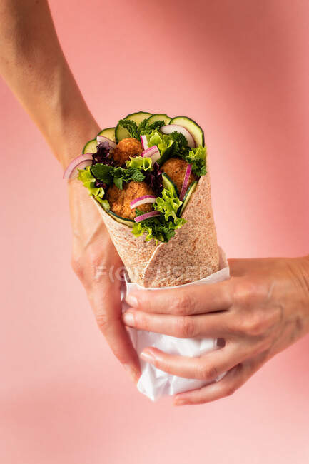 Cropped unrecognizable person hands holding vegan falafel wrap on colorful pink background — Stock Photo