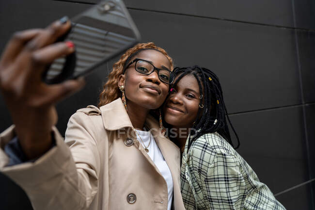 Jeunes afro-américaines souriantes amies se tenant près et prenant autoportrait sur téléphone mobile — Photo de stock