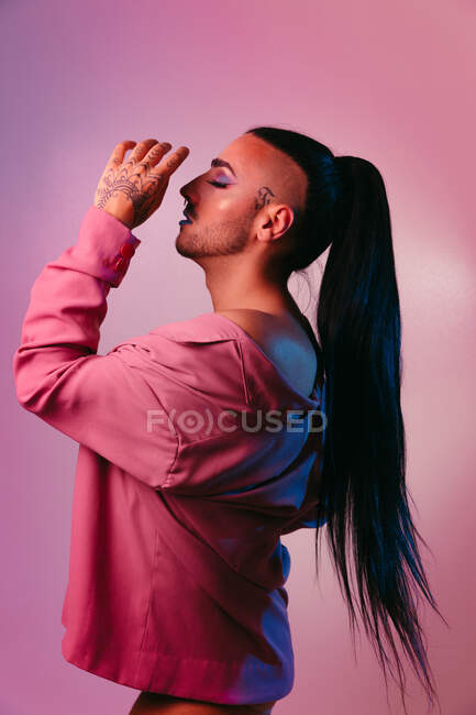 Vista laterale ritratto di glamour transgender donna barbuta in sofisticato make up e occhi chiusi in posa contro sfondo rosa in studio — Foto stock