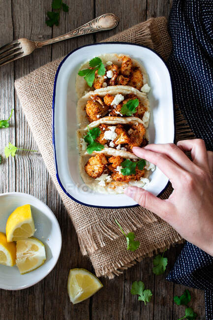 From above hand with cauliflower snack tacos in bowl and lemon pieces in plate on wooden table — Stock Photo