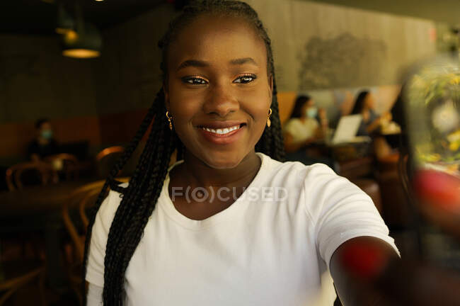 Charmante Afroamerikanerin mit Zöpfen, die im Café Selbstaufnahmen macht und lächelt — Stockfoto