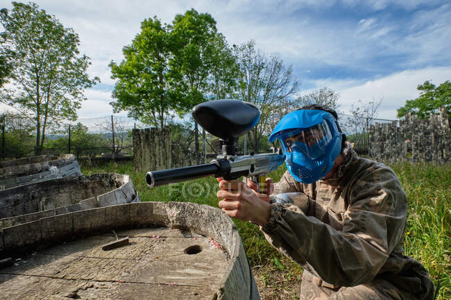 Male player in helmet and camouflage outfit aiming away during paintball game in countryside — Stock Photo